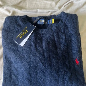 Marinblå stickad tröja Polo Ralph Lauren - 🔹Ralph Lauren stickad polotroja - tidlös klassiker kille🔹  Elegant stickad polotröja fràn Ralph Lauren, perfekt för dig som uppskattar klassisk design med en touch av lyx. Tröjan ar tillverkad i mjukt, högkvalitativt garn som ger både värme och komfort. Den karakteristiska polokragen skapar en sofistikerad silhuett och gör plagget mängsidigt - lika snyggt till vardagsjeans som till en mer uppklädd look.  *   Märke: Ralph Lauren *   Modell: Stickad polotröja *   Färg: [blå] *   Storlek: [small] 