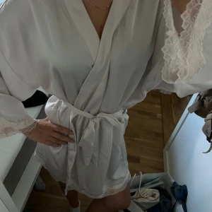 Satin robe med spetsdetaljer - Superfin vit robe i satinliknande material med spetsdetaljer vid ärmslut och nederkant. Har nån liten fläck men inget som syns🤍🤍