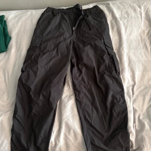 Svarta cargobyxor från Uniqlo M - Svarta cargobyxor från Uniqlo med elastisk midja och snörning. Byxorna har flera praktiska fickor på sidorna och är tillverkade i en mix av bomull och polyamid. Perfekta för en avslappnad och funktionell stil.