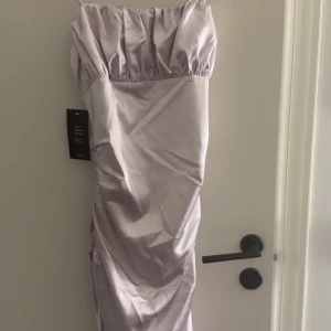 Ljuslila långklänning i satin - Säljer en elegant ljuslila långklänning från NA-KD i glansigt satinmaterial. Klänningen har smala axelband, rynkade detaljer upptill och längs sidorna samt en figurnära passform. Perfekt för dig som vill sticka ut med en stilren look.