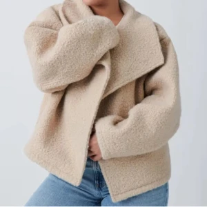Beige teddyjacka med oversized krage - Supermjuk och fluffig teddyjacka i beige med oversized passform och bred, asymmetrisk krage. Jackan har långa ärmar och är perfekt för dig som vill ha en mysig och trendig look.