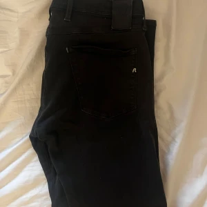 Svarta Replay Anbass jeans 34/32 - Säljer ett par svarta Replay Anbass jeans i storlek 34/32. Klassisk femficksmodell med Replay-logga på fickan och snygga detaljer. Jeansen har en slim passform och är tillverkade i mjukt bomullsmaterial med stretch för extra komfort.