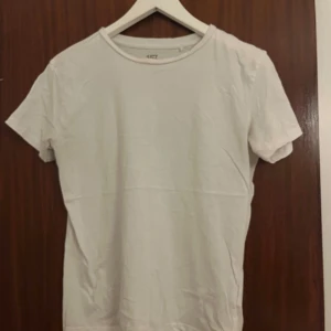 Vit t-shirt från 157 i bomull - En enkel och fräsch vit t-shirt från 157 i storlek S. Modellen är klassisk med rund hals och korta ärmar, tillverkad i 100% bomull för skön känsla. Perfekt att matcha med jeans eller shorts för en clean look.