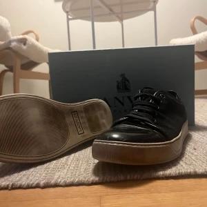Svarta sneakers från Lanvin - Snygga marinblåa sneakers från Lanvin med vit sula och klassisk rund tå. Skorna har snörning och en stilren design med både glansiga och matta partier. Perfekta för dig som gillar exklusiva och tidlösa sneakers med en lyxig känsla.