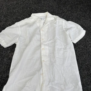 Vit linneskjorta från Lindbergh - Vit kortärmad skjorta från Lindbergh i relaxed fit. Skjortan är tillverkad i svalt linne och har klassisk krage samt knäppning framtill. Perfekt för varma dagar när du vill ha en clean och stilren look.