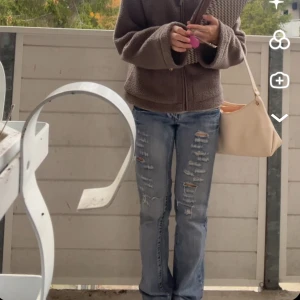 Blå slitna bootcut jeans - Säljer ett par blå jeans med slitningar och hål framtill. Jeansen har bootcut-modell med lätt utsvängda ben och normal passform. Vintage