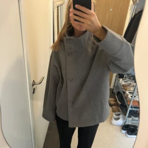 Grå skepparkavaj med stora knappar - Säljer en grå skepparkavaj i ullblandning med oversized passform. Jackan har stora knappar framtill och hög krage som kan bäras både uppfälld och nedvikt. Perfekt för dig som gillar en stilren och chill look.