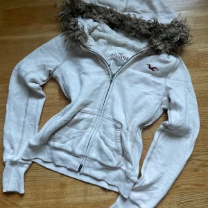 Vit hollister Zip up med päls  - Säljer denna fina hollister tröjan i storlek M, men  passar S då modellen är gammal.  Den har fantastisk päls runt luvan i perfekt skick.  Passar perfekt inför kommande årstider!💕 Vid fler frågor hör av dig!