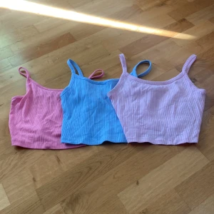 3-pack ribbade croppade linnen - Säljer tre stycken ribbade linnen. Ett ljusrosa, ett babyblått och ett rosa linne, alla med smala axelband och enkel, stilren design. Snygga att matcha med jeans eller shorts för en chill look. Den i starkare i rosa är inte samma som de andra men alla är korta och är i storlek xs. 30 kr för alla 