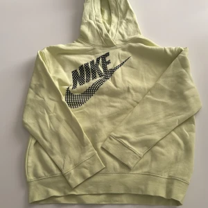Gul hoodie från Nike med tryck - Snygg ljusgul hoodie från Nike med svart logga och coolt prickigt swoosh-tryck på bröstet. Mjuk insida, huva och långa ärmar. Perfekt för dig som gillar streetwear och vill sticka ut lite extra.