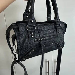 Svart axelväska i ”läder” med detaljer - Säljer denna underbara väskan som är identisk till en märkesväska! Den är väl använd men har inta fel! Köpte den för ungefär 2000 kr!