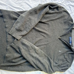 Grå half zip tröja Polo Ralph Lauren - Mörkgrå långärmad tröja från Polo Ralph Lauren med half zip-dragkedja och broderad logga på bröstet. Tröjan är stickad och har ribbade muddar vid ärmslut och nederkant. Perfekt för lager-på-lager och snygg till jeans.