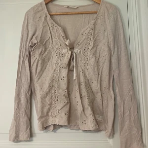 Beige blus med spets och knytband - Supersöt beige blus från Odd Molly med broderade blommor, spetsdetaljer och v-ringning. Långärmad modell med knytband framtill och fina hålbroderier. 