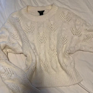 Vit stickad tröja från Lindex - Supermysig vit stickad tröja från Lindex med flätstickat mönster och breda ribbade muddar. Tröjan har rund halsringning och lång ärm, perfekt för lager på lager under kyliga dagar.