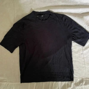 Svart kortärmad tröja från 157 - En stilren svart tröja från 157 med korta ärmar och rund halsringning. Tröjan är i mjuk bomull och har ribbade detaljer vid hals och nederkant. Perfekt för en clean och enkel look.