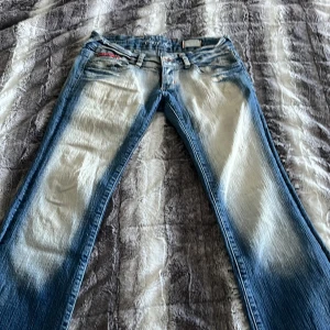 Blå jeans från Crazy Age med brodyr - Säljer ett par blå jeans från Crazy Age med ljusa slitningar och broderade detaljer på bakfickorna. Jeansen har klassisk femficksdesign, dragkedja och knapp framtill samt tydliga kontrastsömmar. Märkespatch bak i midjan och cool faded effekt. Finns en skada (se bild) jag personligen hade inte tänkt på de om man gick runt i sånna här fina byxor. Midjemått är 36 och innerbenslängd är ungefär 80. Lite svårt att veta exakt