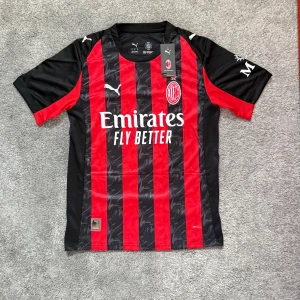 AC Milan Puma fotbollströja Leão #10 - AC Milan matchtröja från Puma med Rafa Leão och nummer 10 på ryggen. Tröjan är röd och svart med klassiska vertikala ränder, broderad Puma-logga och klubbmärke. Tillverkad i lätt och ventilerande polyester, perfekt för fotbollsplanen eller läktaren.