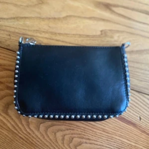 Väska - Svart väska med avtagbart band. Den har silvrigt band och detaljer. Vissa stygn har gått upp men inget som stör funktionen. 