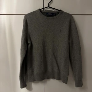 Grå stickad tröja från Polo Ralph Lauren - Snygg grå stickad tröja från Polo Ralph Lauren med klassisk rund halsringning och diskret broderad logga på bröstet. Perfekt basic med lång ärm och mjukt material som passar till allt. Står i tröjan att är en storlek M men har blivit fel tvättad så är mer en S/XS nu