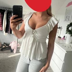 Vit blus med volangärmar och knyt - Supersöt vit blus med volangärmar och v-ringning. Toppen har knyt framtill och är tillverkad i ett lätt, luftigt bomullstyg. Perfekt för en fräsch och somrig look med jeans eller kjol.