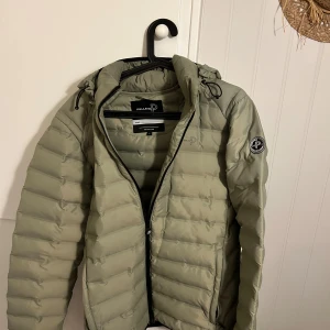 Ljusgrön dunjacka från Pelle P, stl L - Snygg ljusgrön dunjacka från Pelle P med huva och dragkedja framtill. Jackan har quiltad design, diskret logga på bröstet och ett rundat Pelle P-märke på ärmen. Perfekt för kyliga dagar och enkel att matcha med olika outfits.