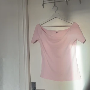 Ljusrosa offshoulder topp - Säljer en ljusrosa topp med offshoulder-design och korta ärmar. Toppen har en mjuk och enkel form som ger en chill vibe, perfekt för att styla med jeans eller kjol. Materialet känns lätt och bekvämt mot huden.