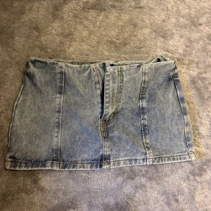 Ljusblå jeanskjol från PrettyLittleThing - Säljer en ljusblå jeanskjol från PrettyLittleThing Petite. Kjolen är kort, har klassisk denimlook med synliga sömmar och dragkedja framtill. Perfekt för dig som gillar en enkel och stilren vibe. Modellen är rak och passar till många olika stilar.