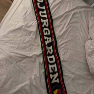 Djurgården Hockey halsduk - Halsduk från Djurgården Hockey med stora vita bokstäver och klubbens klassiska sköld i gult, rött och blått. Nypris 249