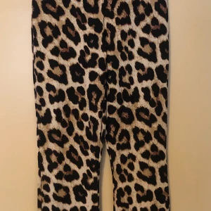 Leopardmönstrade byxor i stretch- lite utsvängda  - Snygga byxor med leopardmönster i svart, beige och bruna toner. Byxorna har rak passform och är tillverkade i ett stretchigt material som sitter bekvämt. Perfekta för dig som vill sticka ut med en djärv look.