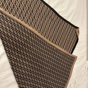 Beige och svart filt - Snygg filt i beige och svart. Rektangulär form med kontrasterande kanter och tätt mönster över hela tyget. Perfekt accessoar för att lyfta din outfit med en lyxig touch.