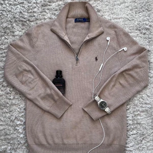 Ralph lauren half zip - Snygg beige stickad tröja från Polo Ralph Lauren med half zip och klassisk broderad logga på bröstet. Tröjan har långärmad passform, ribbade muddar och hög krage. Perfekt nu för lite kyligare dagar för dig som fortfarande vill se stilren ut.