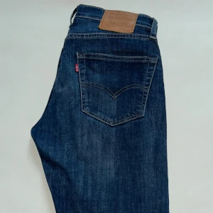 Levi's 502 mörkblå jeans W29 L32 - Snygga Levi's 502 jeans i mörkblå tvätt med klassisk femficksdesign och brunt läderpatch bak. Jeansen har raka ben och normal passform, tillverkade i slitstarkt denim med subtila slitningar för en cool look.