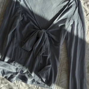 Ljusblå långärmad topp Gina Tricot - Supersnygg ljusblå långärmad topp från Gina Tricot med knyt framtill. Toppen har en djup v-ringning och är gjord i mjuk bomull, perfekt för att lyfta vilken outfit som helst. Säljes i storlek XXS.