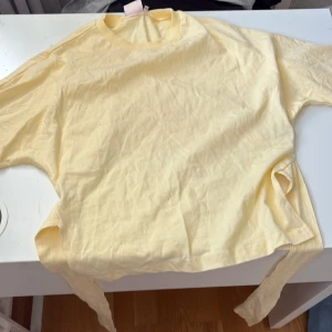 Gul topp med knyt från Nelly - Säljer en ljusgul topp från Nelly i storlek XXS. Toppen har rund halsringning, långa ärmar och knytband i sidorna för en snygg detalj. Tillverkad i mjuk bomull, perfekt för vår och sommar. Enkel och fräsch stil som passar till mycket.