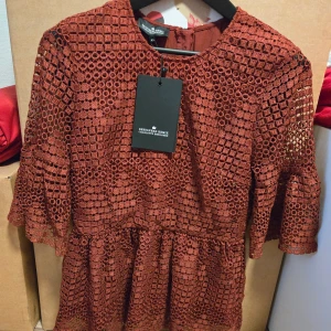 Oxröd klänning helt ny - Superfin oxröd kortklänning med unikt hålmönster och volangärmar. Klänningen har rund hals, dragkedja bak och är tillverkad i ett strukturerat tyg som ger en cool look. Perfekt för dig som vill sticka ut med stil.