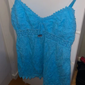 Turkos broderad linnetopp med spets - Supersöt turkos linnetopp med tunna axelband och broderade detaljer över hela toppen. Spetskant upptill och nertill samt en liten knytning framtill med dekorativa pärlor. 