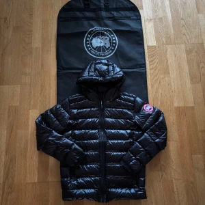 Canada Goose Crofton - Säljer en svart pufferjacka från Canada Goose med huva och klassisk logga på ärmen. Jackan har blanka, quiltade paneler, reflex på huvan och dragkedja framtill. Perfekt för kalla dagar och har en modern, loose passform. Kommer med original fodral och etiketter. Fick som present men tyckte att det inte var en bra passform på mig.   Om ni undrar något skriv pv.                                Vid snabb affär kan gå ner i pris.