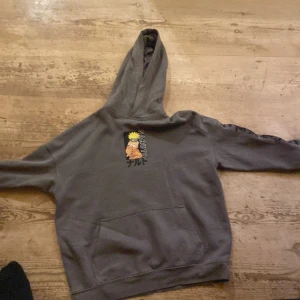 Grå Naruto hoodie från H&M - Säljer en grå hoodie från H&M med Naruto-tryck både fram och bak. Tröjan har stor huva, magficka och långa ärmar. Materialet är mjuk bomullsmix, perfekt för dig som gillar anime och vill ha en chill stil.