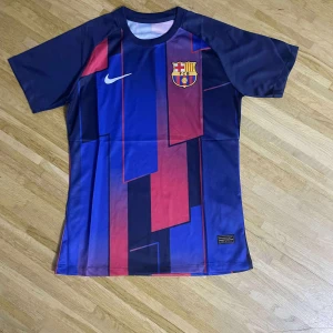 FC Barcelona Nike fotbollströja blå/röd - Snygg FC Barcelona fotbollströja från Nike med klubbmärke på bröstet. Tröjan har korta ärmar och ett grafiskt mönster i blått och rött med inslag av mörkare toner. Tillverkad i lätt och ventilerande material, perfekt för match eller träning.