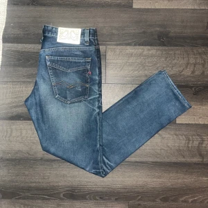 Replay jeans  - Säljer ett par klassiska replay jeans i blå tvätt med snygga slitningar och raka ben. Jeansen har coola detaljer på bakfickorna och är tillverkade i 100% bomull. Perfekt för dig som gillar en tidlös och avslappnad look. Midja 42cm, längd 105cm. JAG SKICKAR INGA FLER BILDER NÄR JAG BÄR JEANSEN :) S2