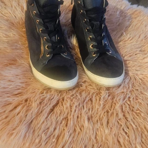 Marinblå höga mocka  sneakers med rosegulddetaljer - Säljer ett par marinblå höga sneakers med snygga roseguldfärgade dragkedjor och öljetter. Skorna har en mix av mocka och skinn, samt mönstrade detaljer vid snörningen. Vita sulor ger en fräsch kontrast. Perfekta för dig som gillar streetstyle och vill sticka ut.