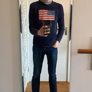 Ralph Lauren USA flagga - Mörkblå stickad tröja från Polo Ralph Lauren med amerikansk flagga och RL-broderi på bröstet. Personen på bilden är 171 och väger 55 kilo. Storleken är 14-16 vilket motsvarar xs-s