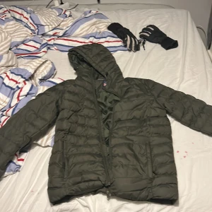 Mörkgrön pufferjacka från Vinson S polo club - Säljer en mörkgrön pufferjacka från Vinson i storlek S. Jackan har huva, dragkedja framtill och två sidofickor. Klassisk quiltad design och badge på ärmen. Perfekt för kalla dagar när du vill hålla stilen och värmen.