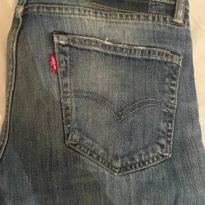 Levi's blå slitna jeans straight fit - Blå jeans från Levi's med klassisk femficksdesign, slitningar och hål på ena benet för en cool, avslappnad vibe. Jeansen har rak passform och tydliga kontrastsömmar. Perfekta för dig som gillar en streetig look.