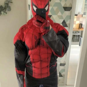 Spiderman dräkt röd och svart - Cool Spiderman kostym i rött och svart med vadderade muskler och detaljerade spindelmotiv på bröstet. Dräkten har helmask och långa ärmar, perfekt för maskerad eller temafest. Snygga svarta och röda kontraster och klassiskt Spiderman-tryck.