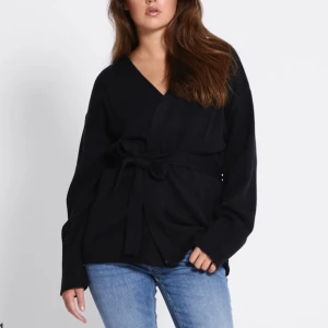 Svart och grå omlottkofta med knytband - Säljer en stilren omlottkofta i svart och ljusgrått med knytband i midjan. Koftan har lång ärm, v-ringning och är tillverkad i mjukt stickat material. Perfekt för lager-på-lager och enkel att matcha med jeans eller kjol. Har både i svart och grå båda finns att köpa 2för 250. svart är st L, gråa M. Är dock själv en st xs/S Går till mitten av rumpan på mig som är 170💕 