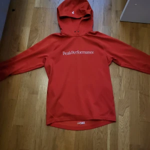 Orange hoodie från Peak Performance - Riktigt snygg orsnge hoodie från Peak Performance med vit logga framtill. Tröjan har huva, långa ärmar och är tillverkad i ett mjukt material som känns skönt mot huden. Perfekt för dig som gillar en sportig och avslappnad stil. Mycket bra skick! 