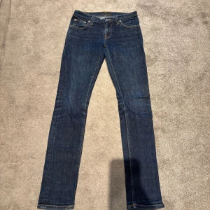 Nudie jeans - Säljer ett par mörkblå jeans från Nudie Jeans med klassisk femficksdesign och snygga kontrastsömmar. Jeansen har rak passform och är tillverkade i slitstarkt bomullstyg. Bakfickorna har Nudie Jeans ikoniska broderi och läderpatch i midjan. Skick 9/10 pris går även att diskuteras