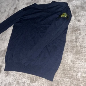 Mörkblå stickad Stone Island tröja - Snygg mörkblå stickad tröja från Stone Island med klassisk patch på vänster ärm. Tröjan har rund hals och långa ärmar, perfekt för dig som gillar stilrena och ikoniska plagg. Passar dig som vill ha en clean look med street-vibe. Pris kan diskuteras! Har vissa defekter.