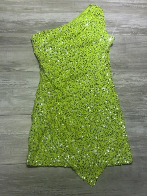 Limegrön paljettklänning Forever New - Säljer en limegrön kort paljettklänning från Forever New. Klänningen är oneshoulder och täckt av glittriga paljetter, med asymmetrisk nederkant och figurnära passform. Perfekt för dig som vill sticka ut och glänsa på nästa fest! Använd en gång bara till nyårs fest.